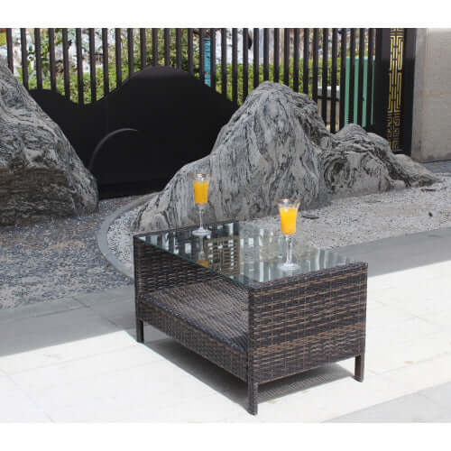 35 inch rectangular coffee table made of brown PE rattan with tempered glass top in an outdoor setting.